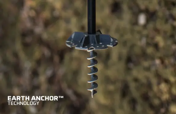 Close-up of a metal earth anchor with a spiral screw design against a blurred outdoor background. Text reads "EARTH ANCHOR TECHNOLOGY" in the bottom left.