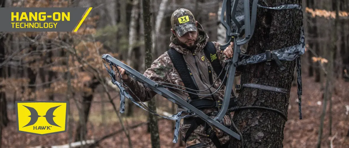 Hunter in camouflage and safety harness ascends tree with a hang-on stand in a dense autumn forest, conveying focus and readiness. "Hang-On Technology" logo visible.