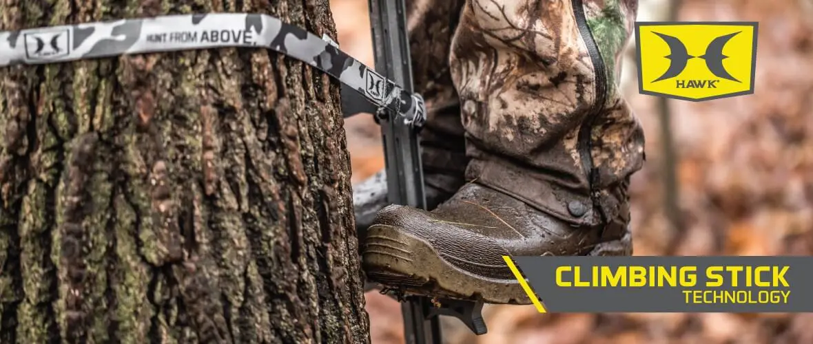A person wearing camo pants and boots uses a climbing stick strapped to a tree. The "Hawk" logo and "Climbing Stick Technology" text are visible.