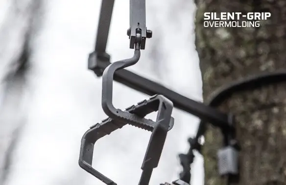 Close-up of a black, textured climbing foothold attached to a tree with a strap. The text "Silent-Grip Overmolding" appears at the top right.